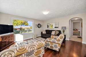 Living area featuring wood-type flooring, a textured ceiling, and arched walkways