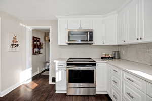 Kitchen with stainless steel appliances, white cabinets, dark wood-style flooring, light stone counters, and tasteful backsplash