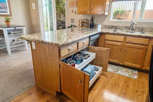 Kitchen featuring brown cabinets, a peninsula, light stone countertops, and light wood-type flooring