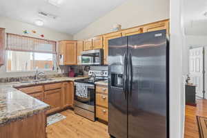 Kitchen featuring stainless steel appliances, light stone counters, light wood-style flooring, a textured ceiling, and vaulted ceiling