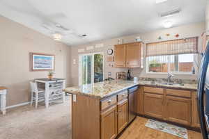 Kitchen with a peninsula, brown cabinetry, light stone countertops, appliances with stainless steel finishes, and a ceiling fan