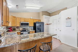 Kitchen with a breakfast bar, stainless steel appliances, a peninsula, lofted ceiling, and light stone countertops