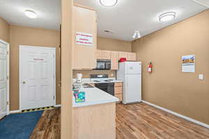 Kitchen featuring light brown cabinetry, light countertops, a textured ceiling, freestanding refrigerator, and range with electric cooktop
