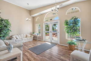 Living room with a chandelier, wood finished floors, french doors, and high vaulted ceiling