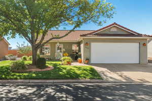 View of front facade featuring stucco siding, a tiled roof, a porch, driveway, and a front lawn