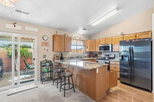 Kitchen featuring light stone countertops, appliances with stainless steel finishes, a peninsula, vaulted ceiling, and a breakfast bar area