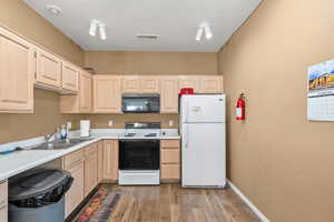 Kitchen with light brown cabinetry, light countertops, white appliances, light wood-style floors, and a textured ceiling
