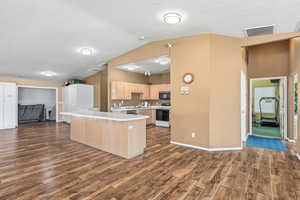 Kitchen with open floor plan, light brown cabinets, light countertops, a textured ceiling, and vaulted ceiling
