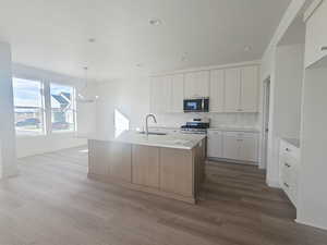Kitchen featuring tasteful backsplash, white cabinets, pendant lighting, a center island with sink, and a chandelier