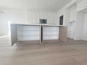 Kitchen with white cabinetry, light countertops, light wood-style flooring, an island with sink, and recessed lighting