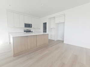 Kitchen with white cabinets, decorative backsplash, stainless steel appliances, a center island with sink, and light wood-style floors