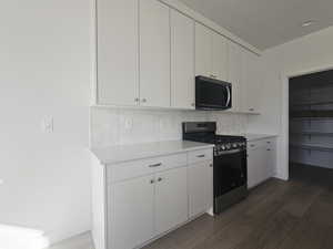 Kitchen with stainless steel gas range, black microwave, white cabinetry, and tasteful backsplash