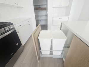 Kitchen with stainless steel stove, light wood-style floors, backsplash, white cabinets, and light stone countertops