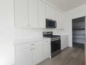 Kitchen with stainless steel appliances, white cabinetry, light wood-style floors, and decorative backsplash