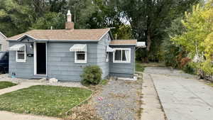 View of front facade featuring roof with shingles, view of scattered trees, a chimney, and a front lawn