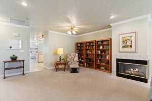 Living area featuring carpet flooring, a textured ceiling, crown molding, a fireplace, and ceiling fan