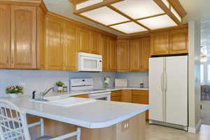 Kitchen with white appliances, light countertops, a peninsula, a kitchen bar, and brown cabinetry