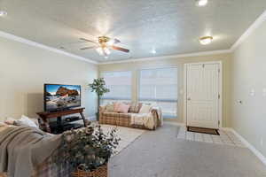 Living room featuring a textured ceiling, ornamental molding, light colored carpet, ceiling fan, and light tile patterned flooring