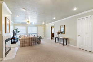 Living area with ornamental molding, light colored carpet, a textured ceiling, a tiled fireplace, and a ceiling fan
