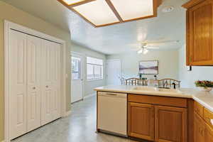 Kitchen featuring brown cabinets, a textured ceiling, light countertops, dishwasher, and a peninsula