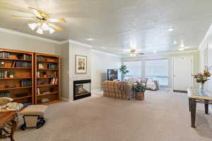 Carpeted living area featuring ceiling fan, ornamental molding, a textured ceiling, and a tiled fireplace