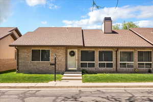 View of front of home with a shingled roof, a front lawn, brick siding, and a chimney