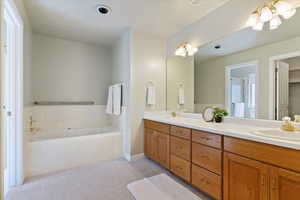 Full bathroom featuring double vanity, a garden tub, light colored carpet, and a chandelier