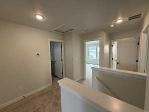 Hall featuring an upstairs landing, light colored carpet, a textured ceiling, and attic access