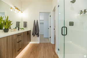Full bath with vanity, light wood-style floors, a walk in closet, and a stall shower
