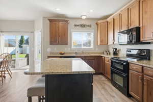 Kitchen with black appliances, a kitchen bar, a kitchen island, light stone countertops, and recessed lighting