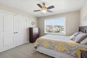 Bedroom featuring light carpet, a ceiling fan, and a closet