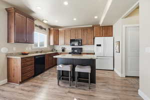 Kitchen featuring black appliances, light stone counters, a breakfast bar area, a center island, and recessed lighting