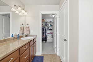 Full bath with vanity, light tile patterned flooring, and a walk in closet