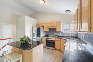 Kitchen with stainless steel appliances, dark stone countertops, light brown cabinets, lofted ceiling, and tasteful backsplash