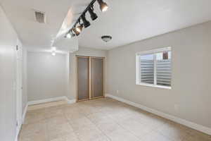 Unfurnished bedroom featuring rail lighting, a closet, and light tile patterned flooring