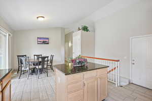 Kitchen featuring light brown cabinets, wood finish floors, dark stone counters, lofted ceiling, and a kitchen island