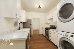 Kitchen with stainless steel appliances, dark wood-style flooring, white cabinetry, light countertops, and stacked washing machine and dryer