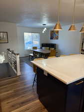 Kitchen with dark cabinets, pendant lighting, a breakfast bar, dark wood-style flooring, and a textured ceiling
