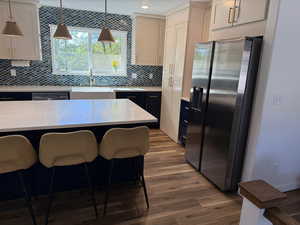 Kitchen with stainless steel appliances, decorative backsplash, dark wood finished floors, pendant lighting, and light stone counters