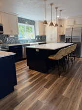 Kitchen with dark cabinets, backsplash, stainless steel appliances, hanging light fixtures, and a center island
