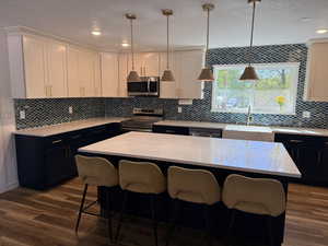 Kitchen featuring a center island, appliances with stainless steel finishes, light stone counters, a textured ceiling, and decorative light fixtures