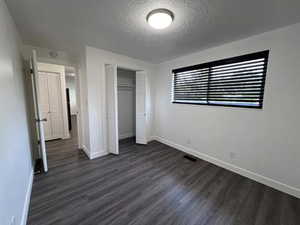 Unfurnished bedroom featuring a textured ceiling, dark wood-style floors, and a closet