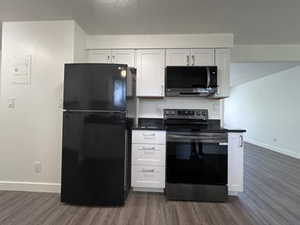 Kitchen with black appliances, dark countertops, dark wood-style floors, white cabinetry, and a textured ceiling