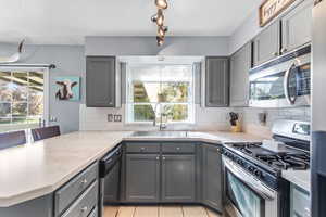 Kitchen featuring gray cabinets, stainless steel appliances, light countertops, a textured ceiling, and light tile patterned floors