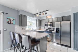 Kitchen featuring light tile patterned floors, stainless steel appliances, decorative backsplash, light countertops, and a kitchen bar