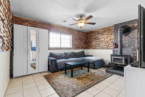 Living room with a wood stove, wainscoting, light tile patterned floors, a textured ceiling, and ceiling fan