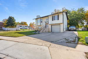 Bi-level home featuring concrete driveway, a chimney, brick siding, and an attached garage
