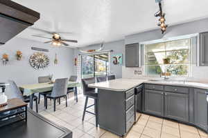 Kitchen with gray cabinetry, a peninsula, light countertops, a textured ceiling, and light tile patterned flooring