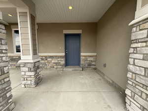 Property entrance with stone siding, covered porch, and stucco siding