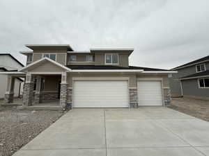 Prairie-style home with stone siding, concrete driveway, a porch, and stucco siding
